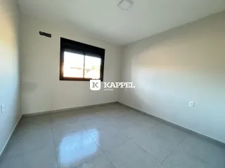 Uma sala de estar clara com piso de porcelanato e uma grande janela.