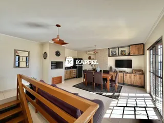 Sala de estar com piso de madeira e área de cozinha visível.