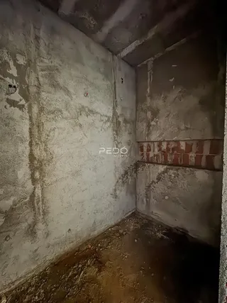 Foto de um espaço interno com paredes de concreto cru e piso de terra.