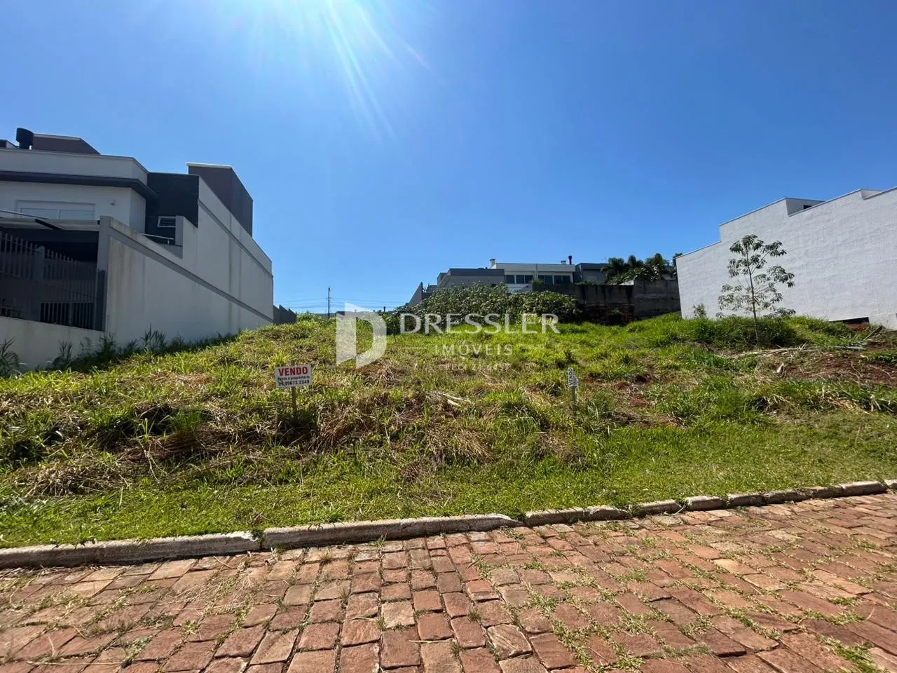 Vista externa de uma propriedade com terreno gramado e edificações brancas no fundo.