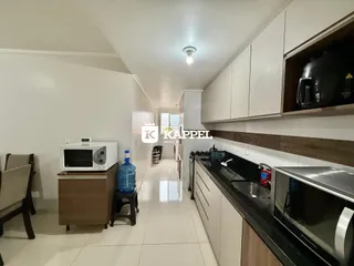 Uma cozinha moderna com armários brancos e bancada escura é vista ao longo de um corredor claro.