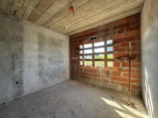 Interior de uma sala em construção com paredes de tijolo aparente e teto de concreto.
