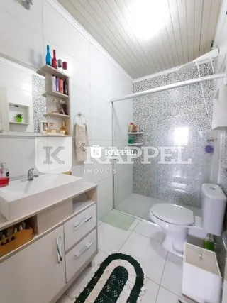 Banheiro com revestimento cerâmico e box de vidro transparente.