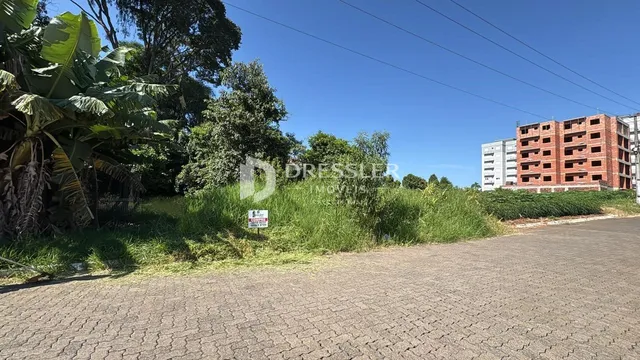 Vista externa de uma propriedade com vegetação densa e um edifício de tijolos ao fundo.