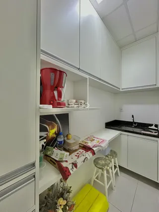 Vista interna de uma cozinha com armários brancos e bancada escura.