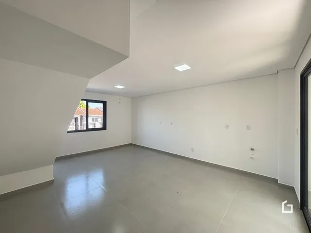 Interior de uma sala ampla com paredes brancas e piso cinza.