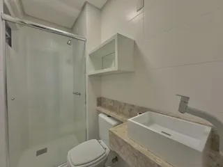 Banheiro com box de vidro, vaso sanitário e bancada de mármore.