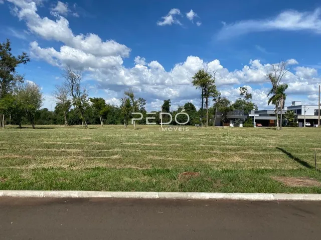 Vista externa de um terreno gramado com árvores e uma estrada no primeiro plano.