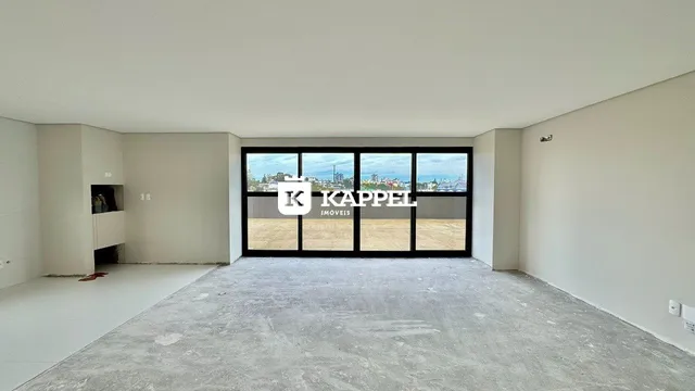Sala ampla com piso de concreto e grandes janelas que dão vista para o exterior.