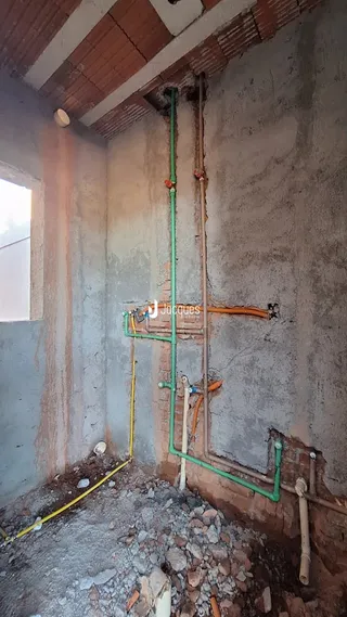 Foto de uma parede interna com tubulações expostas em construção.