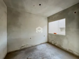 Interior de um cômodo com paredes e piso em estado bruto.