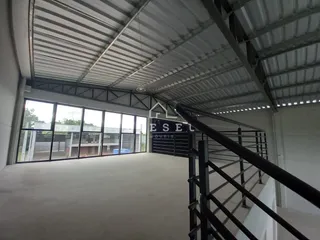 Vista interna de um grande espaço industrial com teto de metal e janelas amplas.