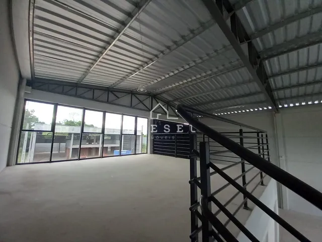 Vista interna de um grande espaço industrial com teto de metal e janelas amplas.