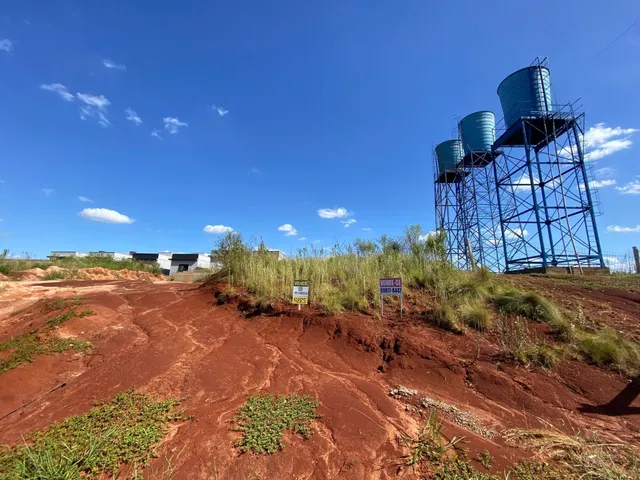 Vista de uma área de terra vermelha com uma estrutura industrial ao fundo.