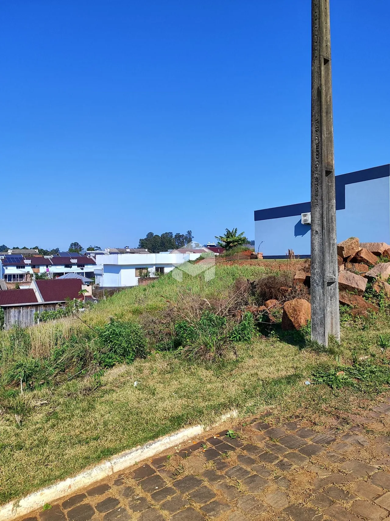 Vista externa de uma propriedade com terreno inclinado e vegetação.