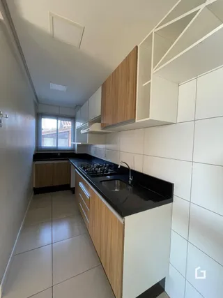Vista interna de uma cozinha com armários de madeira e revestimento branco.