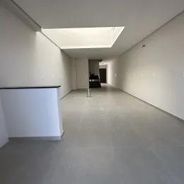 Um corredor longo e vazio com paredes brancas e piso cinza claro.