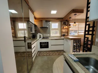 Vista interna de uma cozinha com armários brancos e detalhes em madeira.