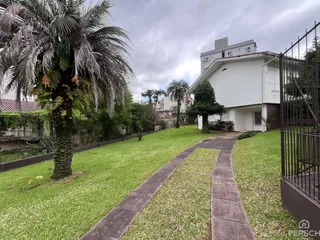 Vista externa de um jardim gramado com uma casa branca ao fundo.