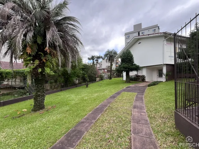 Vista externa de um jardim gramado com uma casa branca ao fundo.