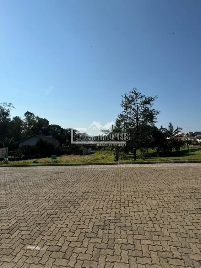 Vista externa de uma área pavimentada com árvores ao fundo.