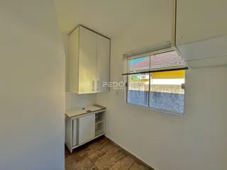 Interior de uma cozinha com armários brancos e piso de cerâmica.