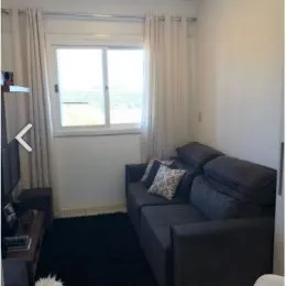 Uma sala de estar com sofá e janelas cobertas por cortinas brancas.