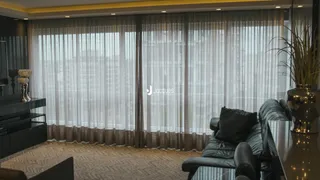 Sala de estar com grandes janelas cobertas por cortinas claras.