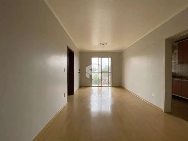 Ambiente interno de uma sala ampla com piso de madeira clara e grande janela.