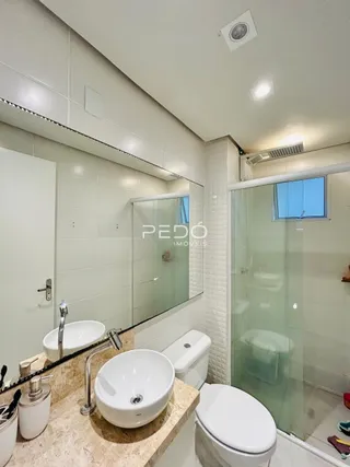 Foto de um banheiro interno com box de vidro e pias brancas.