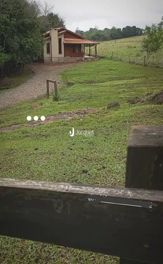 Vista da fachada de uma casa em uma área rural com gramado e colinas ao fundo.