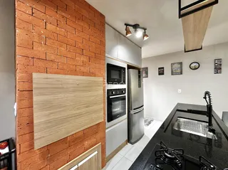 Interior da cozinha com parede de tijolos aparentes e armários brancos.