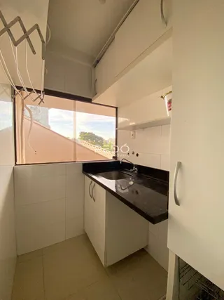 Vista interna de uma cozinha com armários brancos e janela.