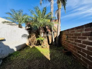 Vista externa de um quintal com paredes de tijolo e vegetação tropical.