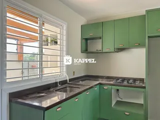 Cozinha moderna com armários verdes e bancada escura em um imóvel no Brasil.