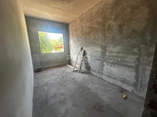 Vista interna de um ambiente com paredes de concreto aparente e piso cru.
