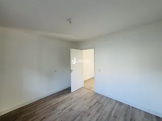 Ambiente interno de uma sala com piso de madeira clara e paredes brancas.