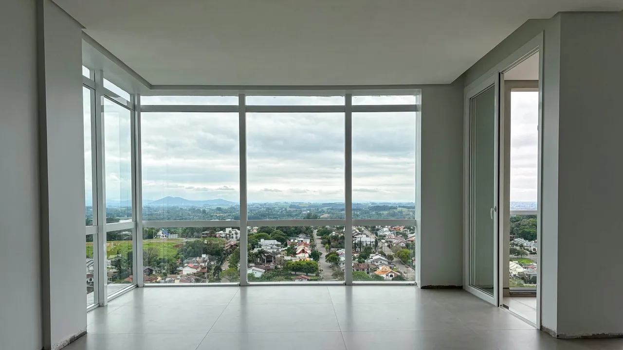 Sala de estar com grandes janelas que proporcionam uma vista panorâmica da paisagem urbana e campos.
