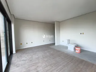 Interior de uma sala ampla com piso de madeira e paredes brancas.