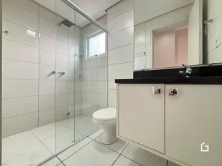 Foto de um banheiro com box de vidro e piso cerâmico branco.