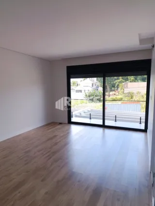 Ambiente interno de uma sala com piso de madeira clara e portas de vidro grandes.