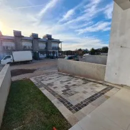 Área externa pavimentada com gramado em frente a um edifício residencial.