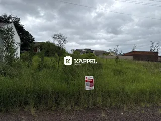 Vista externa de um terreno com vegetação alta e sinalização de imobiliária.