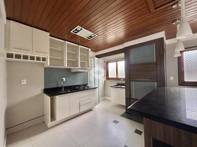 Vista interna de uma cozinha com teto de madeira e armários brancos.