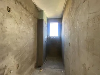 Corredor estreito com paredes de concreto aparente e uma janela no final.