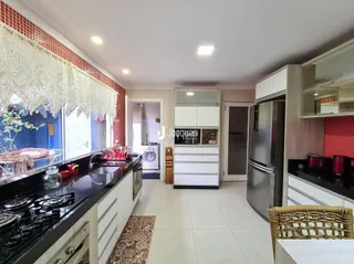 Vista interna de uma cozinha com armários brancos e bancadas escuras.