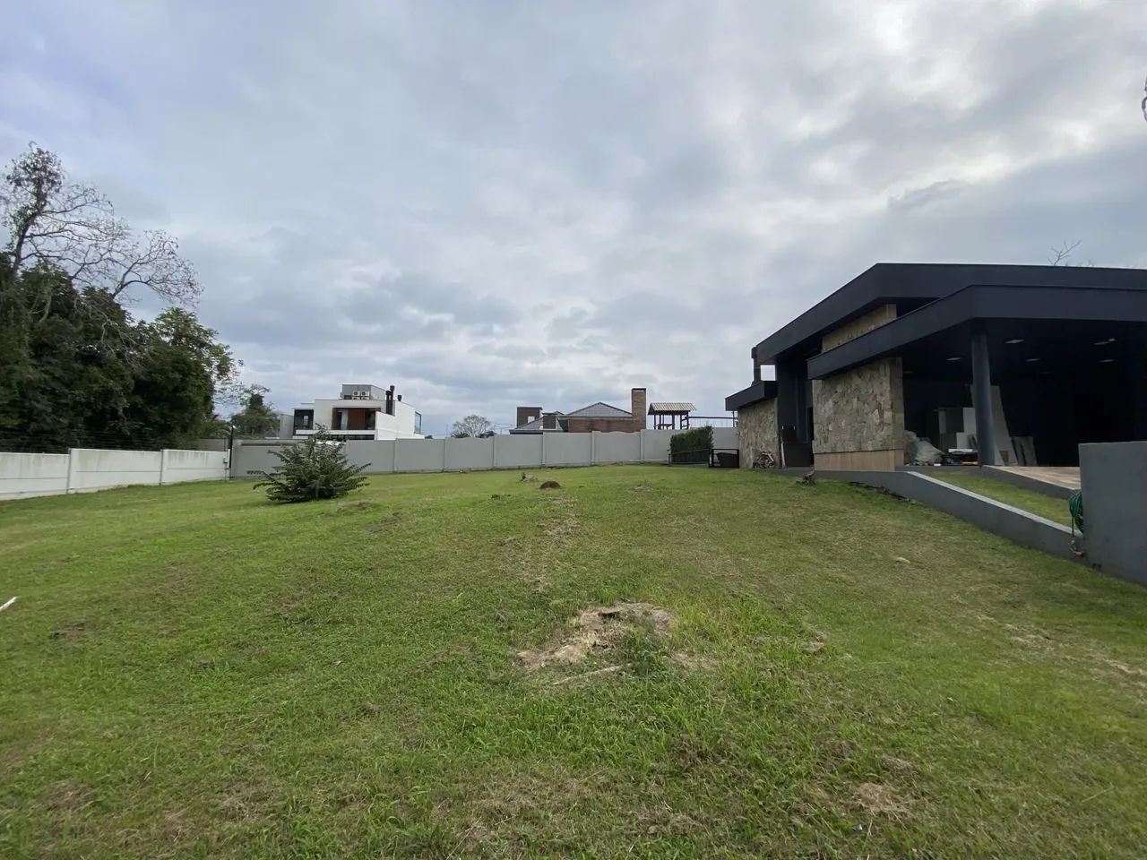 Vista externa de um terreno gramado com uma casa moderna ao fundo.