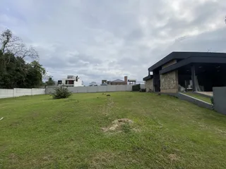 Vista externa de um terreno gramado com uma casa moderna ao fundo.