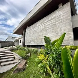 Fachada de um edifício moderno com revestimento de pedra e vegetação no primeiro plano.