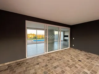 Vista interna de uma sala com piso de ladrilhos e portas de vidro que dão acesso a uma área externa.